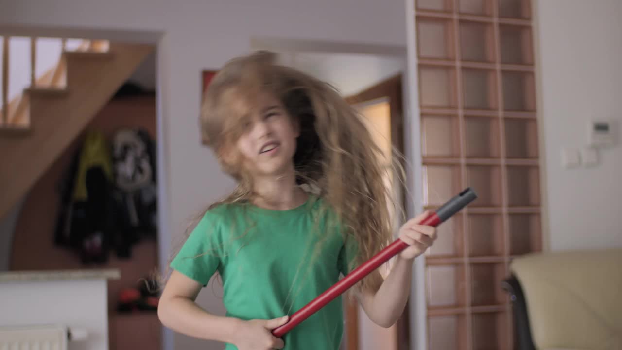 享受清洁俏皮创意儿童舞蹈。创意少女家庭主妇用扫帚把当吉他打扫唱歌，孩子用拖把当乐器在家里唱歌。视频下载