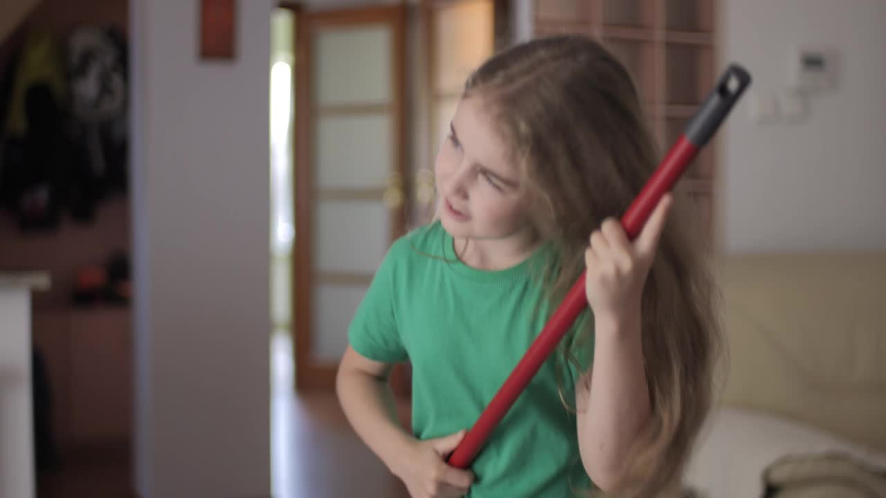 享受清洁俏皮创意儿童舞蹈。创意少女家庭主妇用扫帚把当吉他打扫唱歌，孩子用拖把当乐器在家里唱歌。视频下载