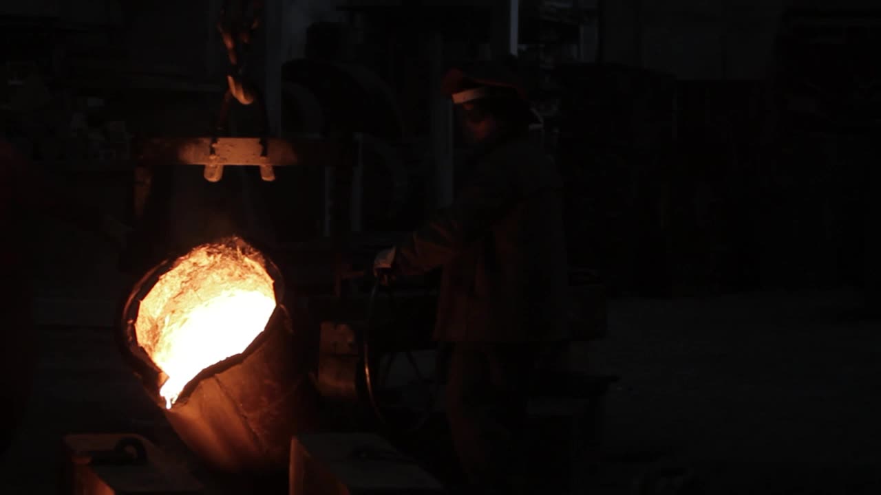 工业工人在铸造厂倾倒熔化的金属。团队在工厂进行铸钢，操作重型机械。车间内的体力劳动，高温操作，金属加工过程。视频下载
