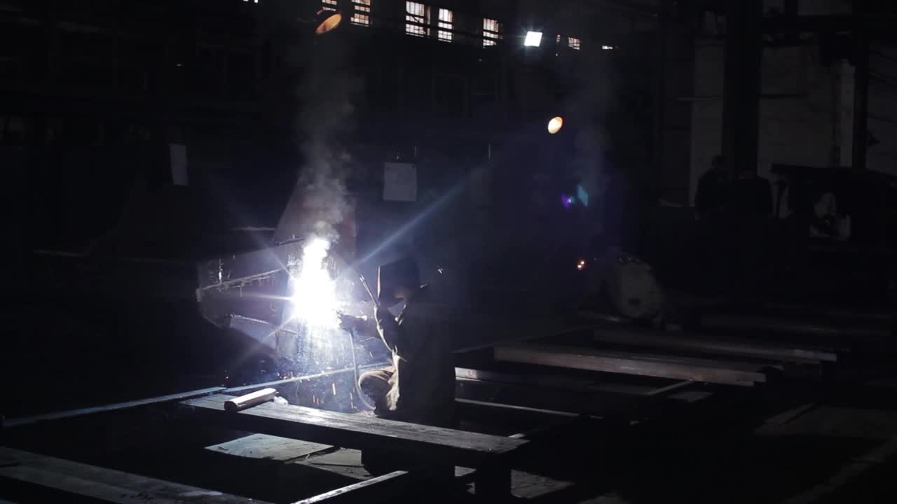 带着防护面具的工业焊工在建筑工地焊接金属，火花从电弧中飞出，熟练的技工在黑暗的车间里做钢细木工，制造工作。视频下载