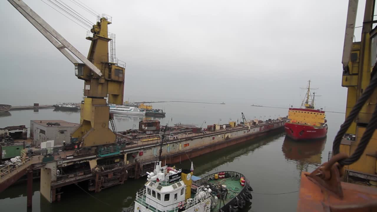 工业港口的景象，起重机将货物装载到船上。拖船辅助船舶航行，在城市港口码头活动。海运，沿海地区物流业务，出口。视频下载