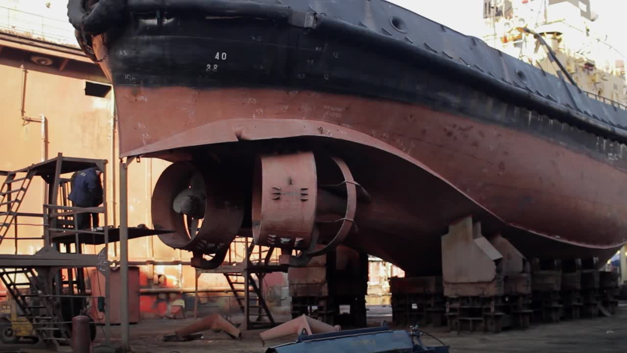 工人在干船坞用焊接、打磨修理船舶。在工业船厂维修船只。戴着头盔修理船体的人，海事工程的壮举。船舶大修、钢结构改造。视频下载