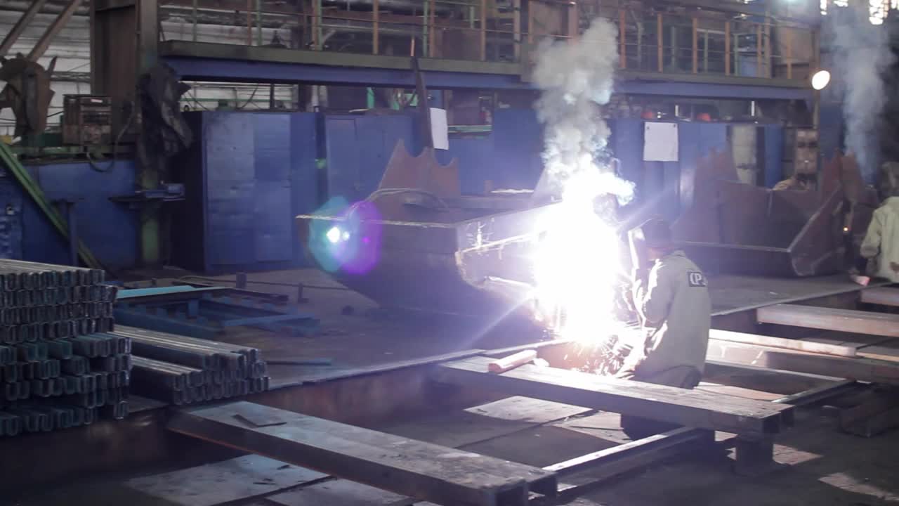 在工厂里，工人戴着防护装备焊接铁梁，火花四溅。精密金属制品，车间钢结构制造。劳动，熟练工艺，安全措施。视频下载