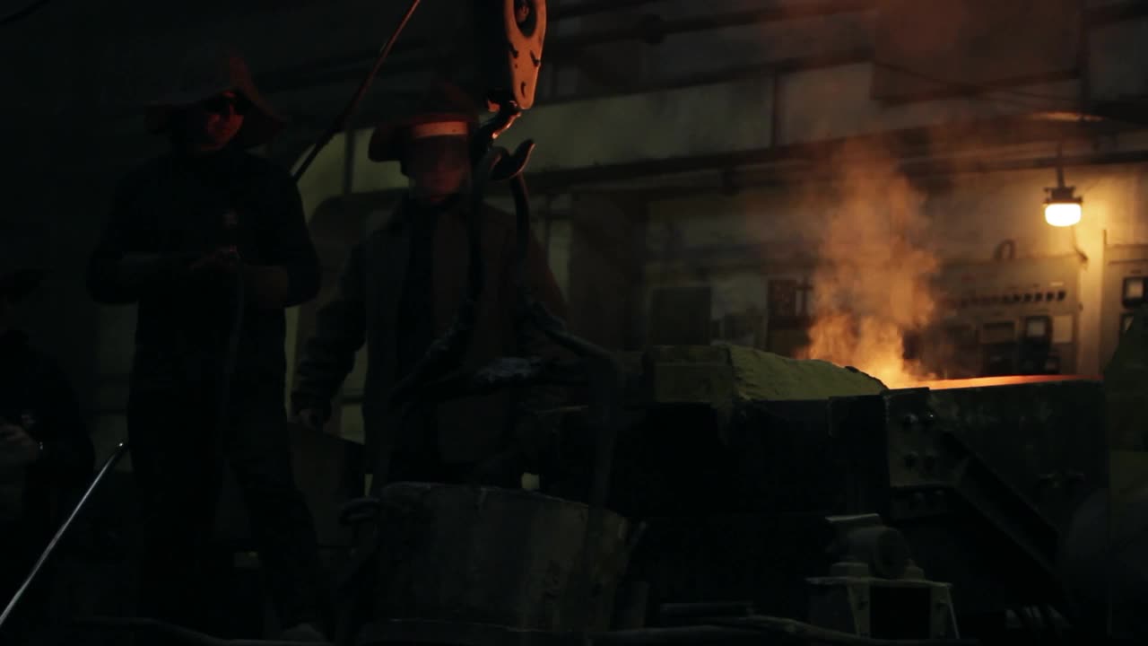 工业工人在铸钢厂倾倒熔化的金属，火焰飞溅，团队在耐热齿轮中操作重型机械，工作场所安全，工厂的金属加工过程，钢铁生产现场视频下载