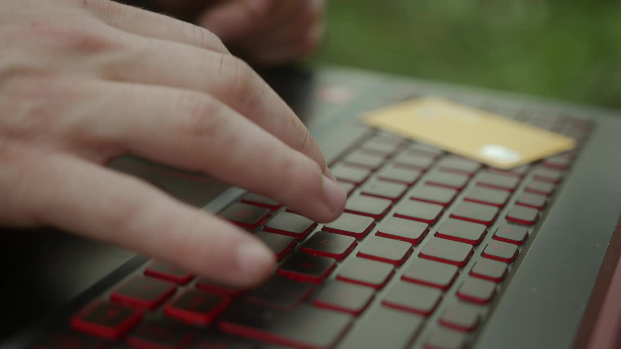 一个年轻人用手在笔记本电脑上打字和用信用卡付款的特写，键盘和信用卡特写视频下载