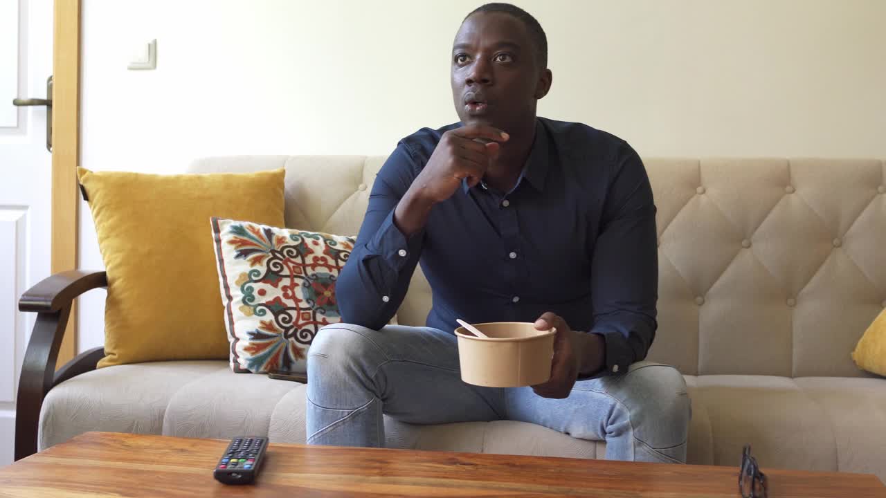 一个男人坐在沙发上，手里拿着一只碗视频下载
