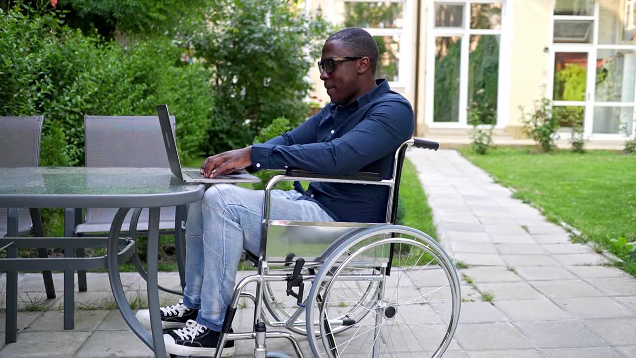 一个轮椅使用者在花园里用他的笔记本电脑打字视频下载