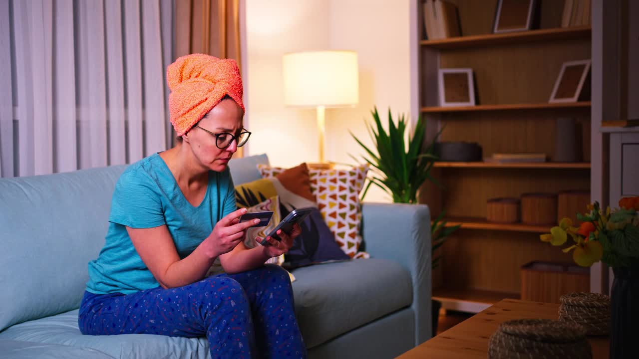 深夜，一个穿着睡衣、头上缠着毛巾的女人坐在沙发上，用手机在网上购物视频下载