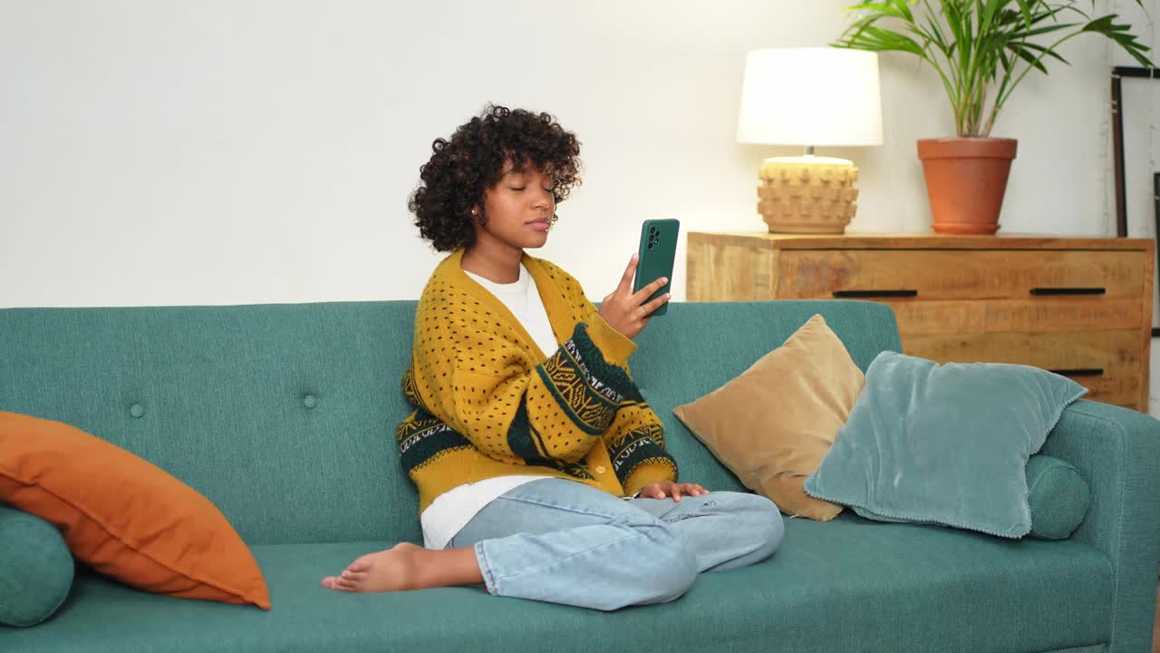 非裔美国女孩拿着智能手机视频聊天。女博主在社交网络上与最好的朋友聊天。年轻女子在家里进行虚拟会议在线聊天视频通话。视频下载
