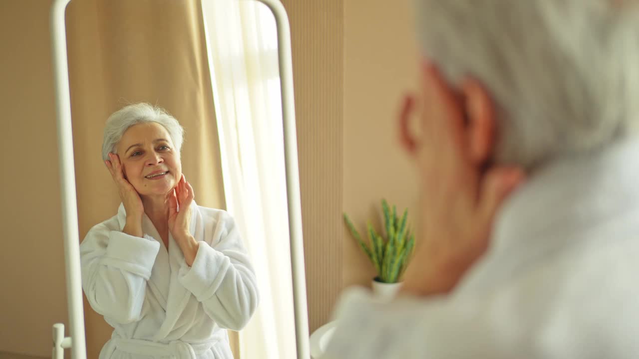 爱你自己。欣赏镜子反射的美丽老妇人。年长的女士在浴室里对着镜子度过了一个充满自信和快乐的早晨。每天早晨做例行美容的女人。自我的爱。视频下载