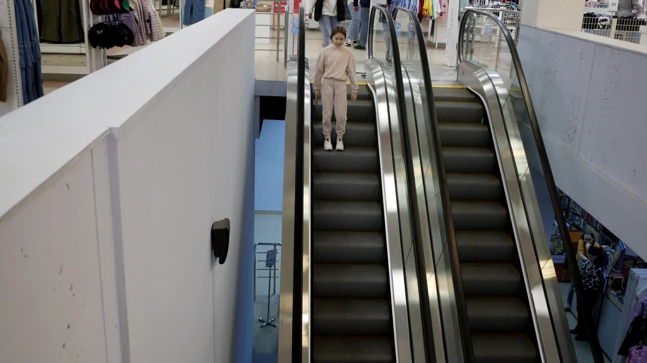 一个女孩乘坐自动扶梯进入地下通道。在商场里，一个小孩乘自动扶梯下楼梯。俯视图视频下载