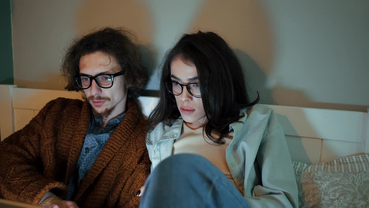 两个全神贯注于笔记本电脑屏幕的人，在床上分享了片刻的数字连接视频下载