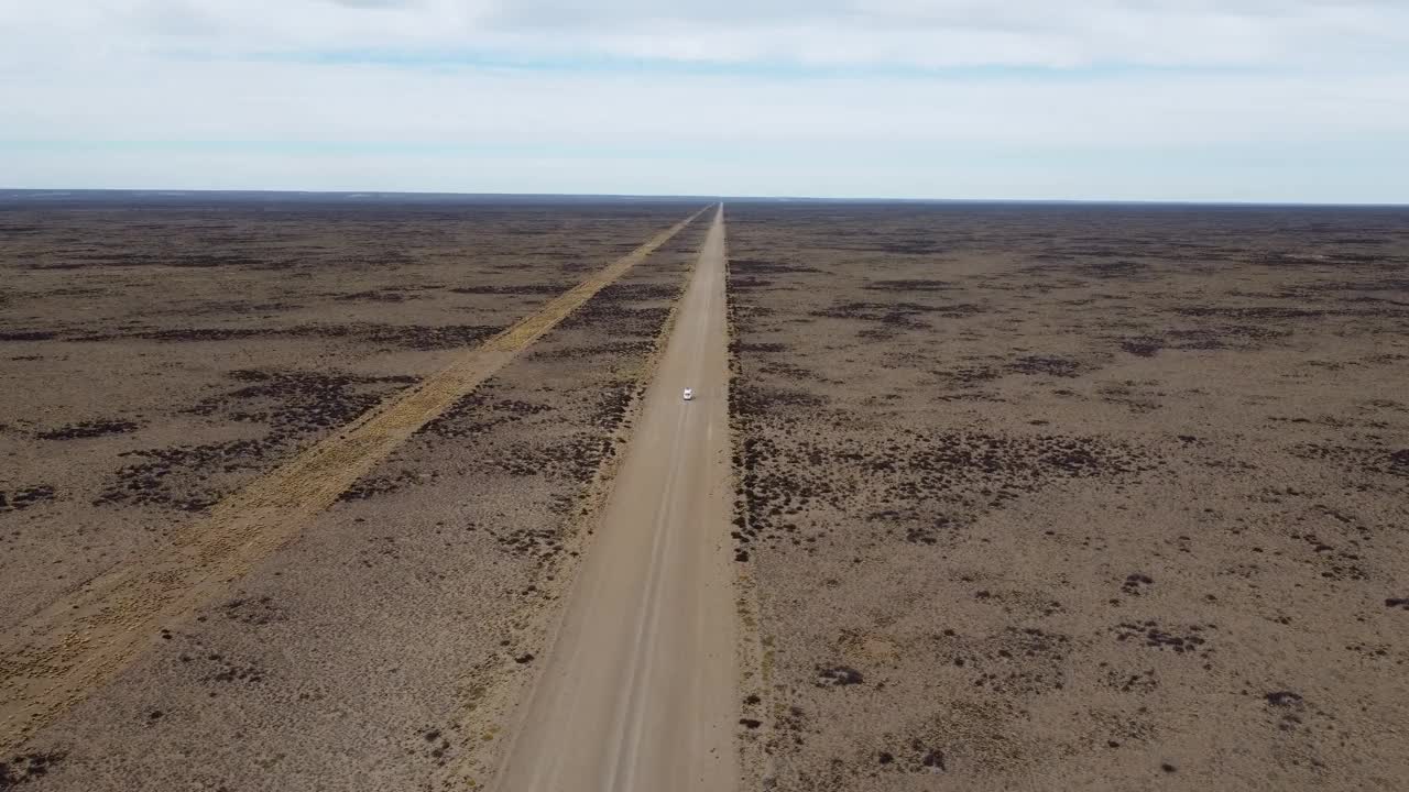 航拍视频显示，一辆白色小货车行驶在平坦干旱的砾石路上视频下载