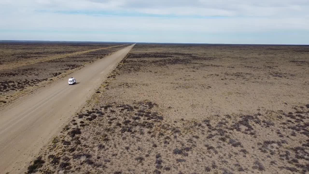航拍视频显示，一辆小型白色面包车在平坦干旱的砾石路上行驶视频下载