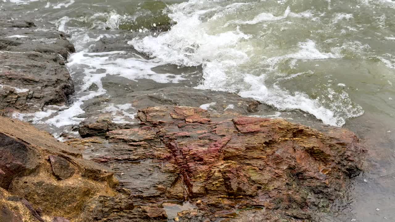 海浪和涟漪冲击着河口处的火山岩，慢慢地侵蚀着岩石视频下载