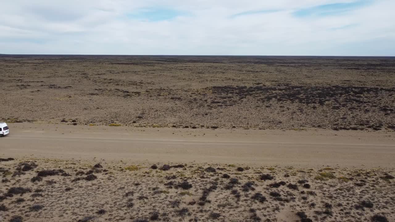航拍视频侧视图的小白色面包车行驶在砾石路平坦干旱景观视频下载