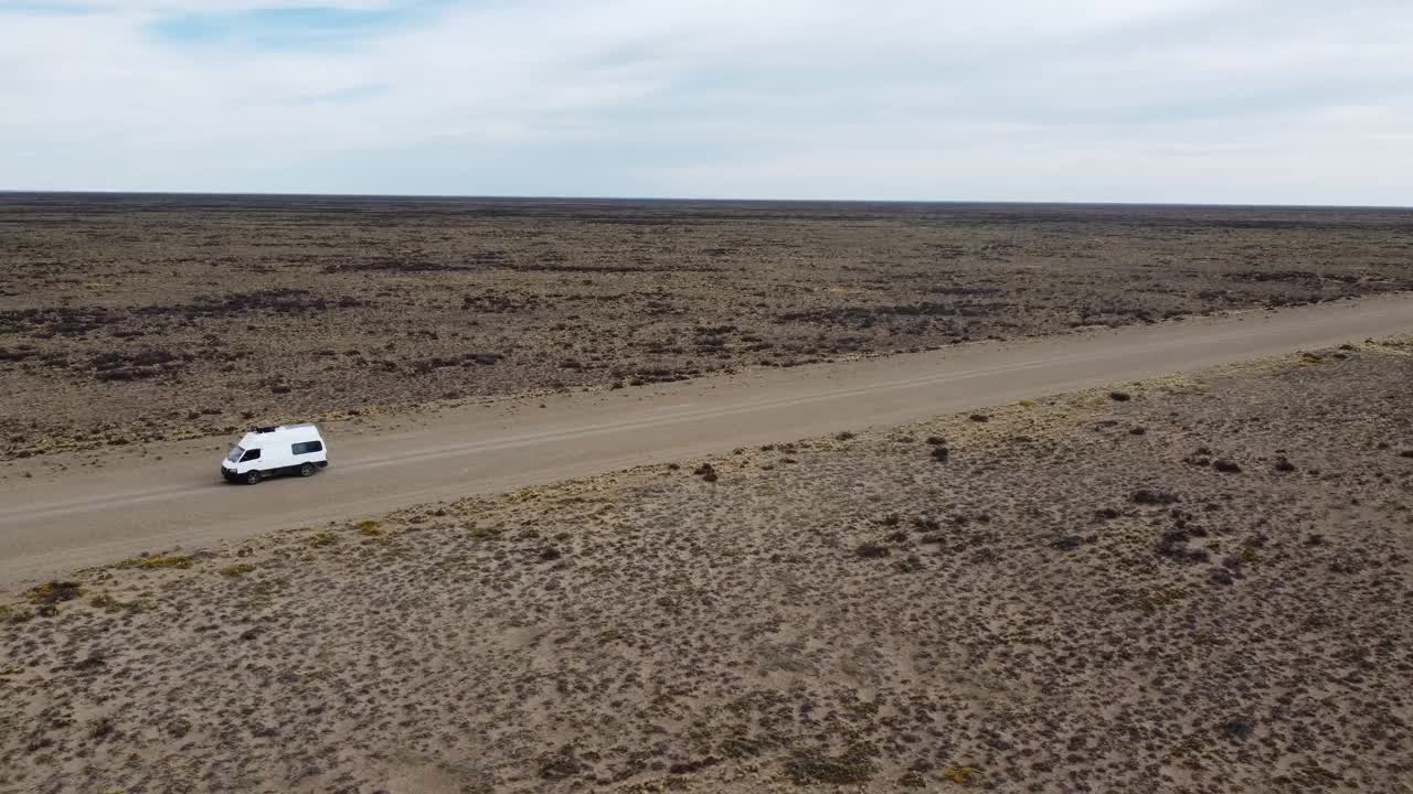 航拍视频显示，一辆白色小货车在平坦干旱的砾石路上行驶视频下载
