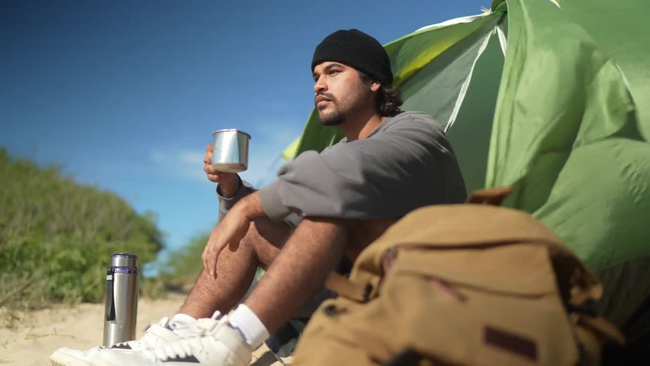 年轻人在海滩上沉思，喝着咖啡视频素材