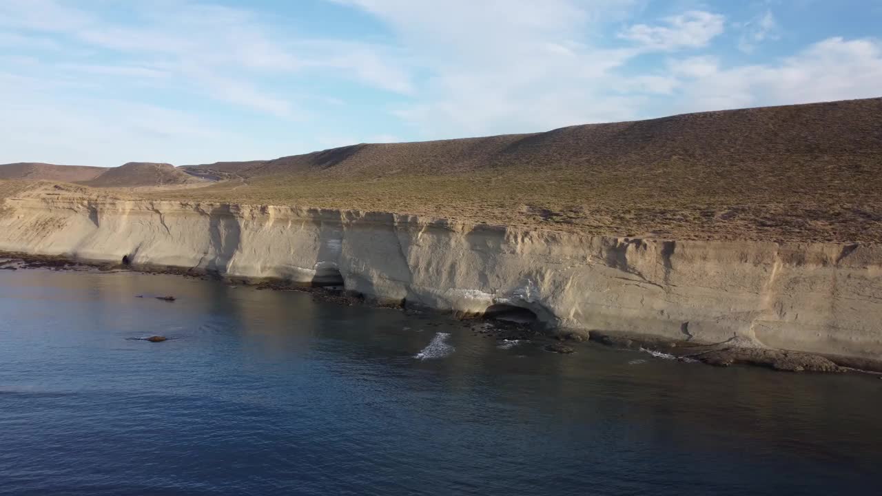 相机从海上沿着巴塔哥尼亚海岸线拍摄，那里有高高的浅棕色悬崖和悬崖上的侵蚀洞穴视频下载