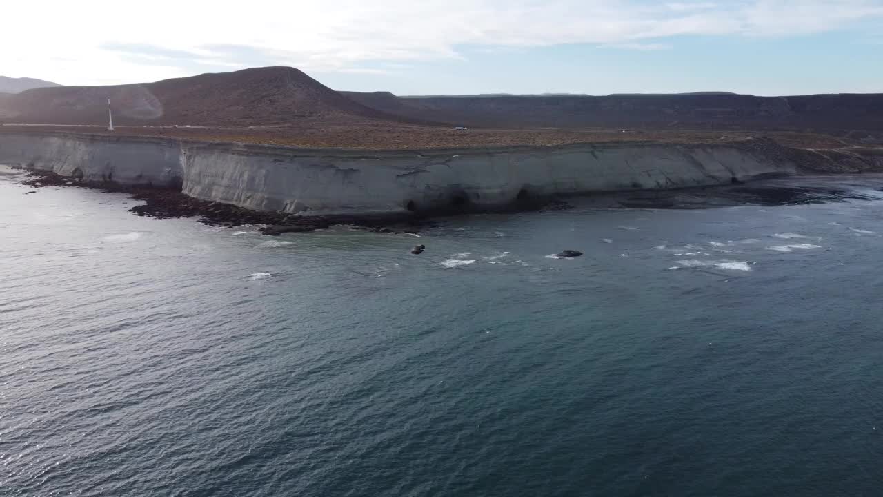 相机从海上望向巴塔哥尼亚海岸线，远处有高高的浅棕色悬崖和高速公路视频下载
