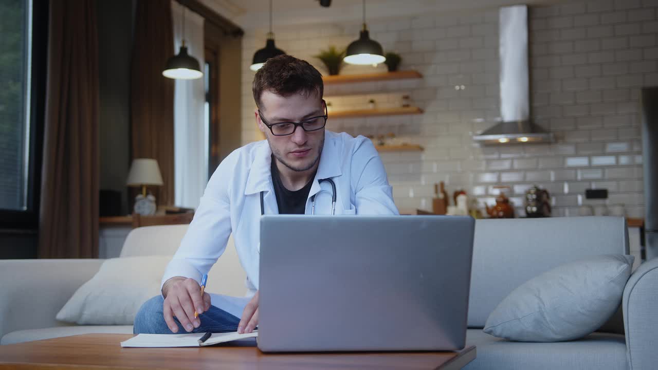 专业的年轻男医生戴着眼镜，穿着白色制服，戴着听诊器，通过笔记本电脑的网络摄像头与患者进行在线会议视频通话。远程医疗咨询视频下载