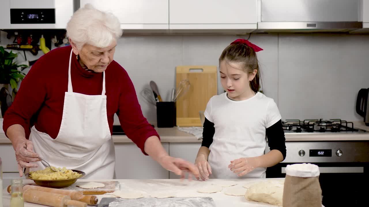 烘烤。奶奶和学妹在厨房做馅饼和包子。教学。孩子在帮着往面团里放馅料视频下载