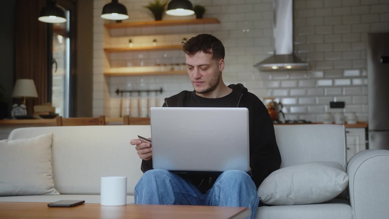 沮丧的男人坐在家里的沙发上，在笔记本电脑上输入信用卡号码，因为网上购物信用卡被拒绝或超过限额，感到悲伤和不高兴视频下载