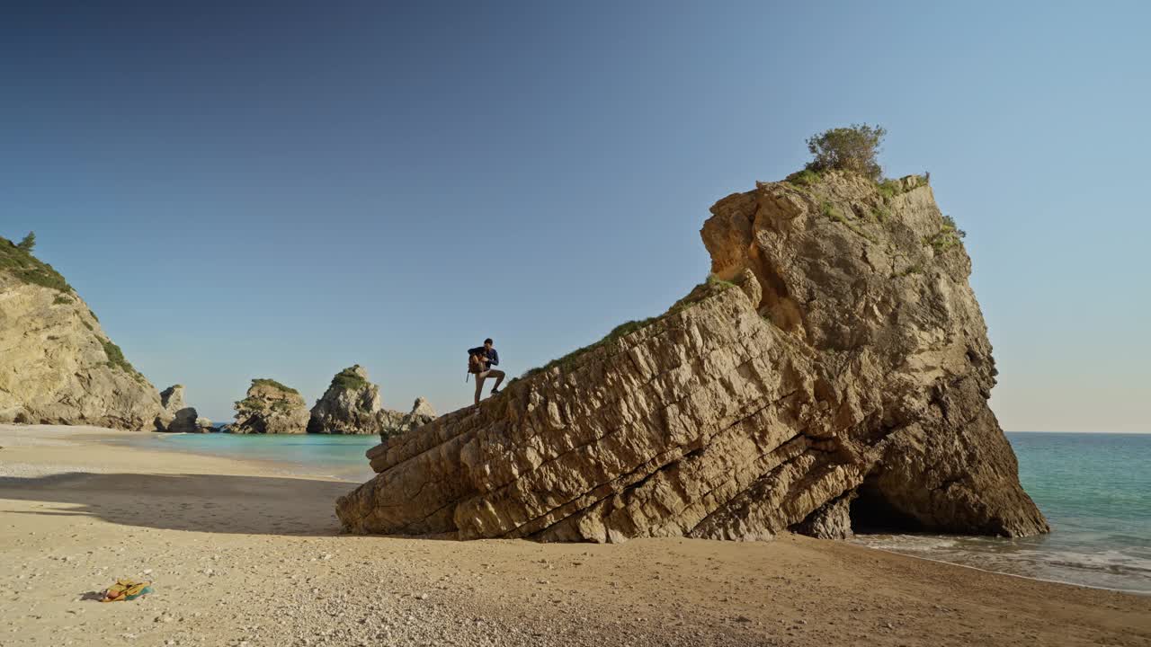 一名男子在塞辛布拉海滩的岩石上用智能手机拍摄视频下载