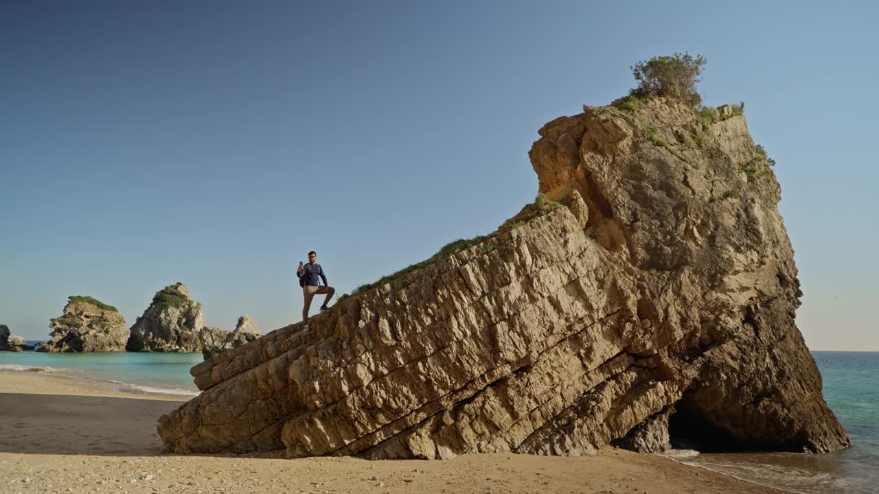 一名男子在塞辛布拉海滩的岩石上用智能手机拍摄视频下载