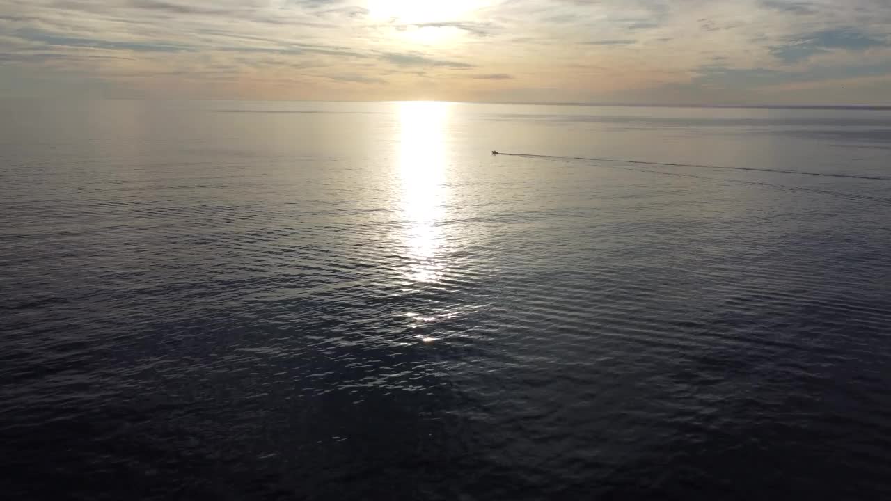 海面上的小船在日出时穿过阳光闪闪发光的海面，镜头正对着太阳视频下载