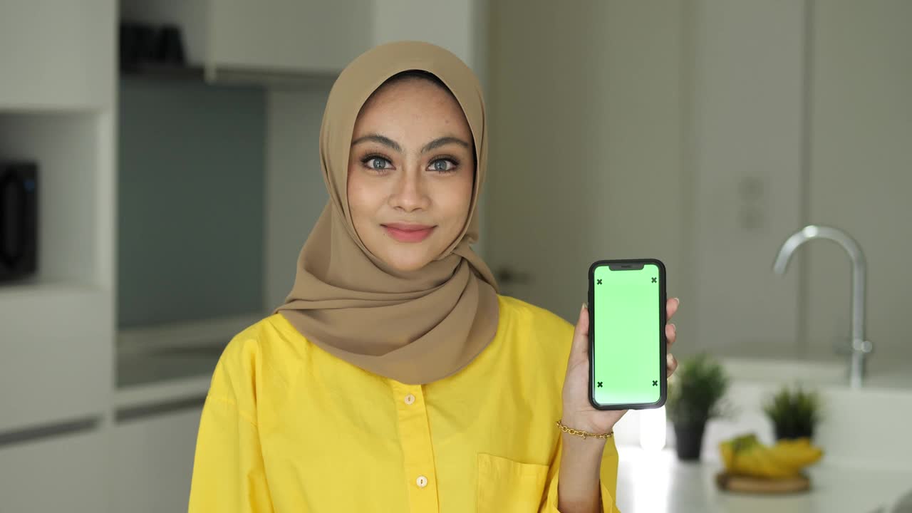 亚洲年轻人投资在线业务。戴头巾的女人指着智能手机微笑着视频下载