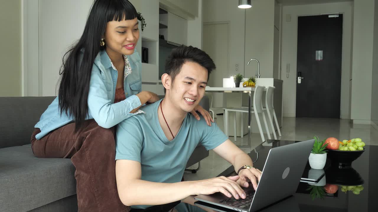 幸福的多种族亚洲夫妇在家里用笔记本电脑工作，处理财务和投资视频素材