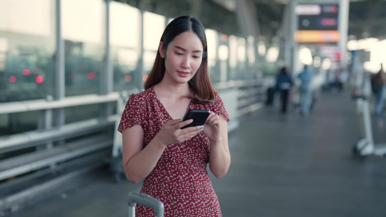 手持智能手机的年轻亚洲女子在熙熙攘攘的机场候机楼等待交通视频下载