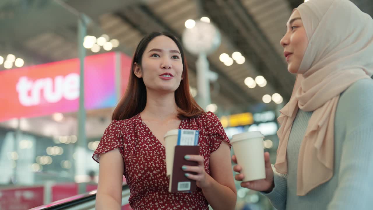微笑的年轻亚洲旅客在机场自动扶梯上拿着咖啡，在前往登机口的途中交谈视频下载