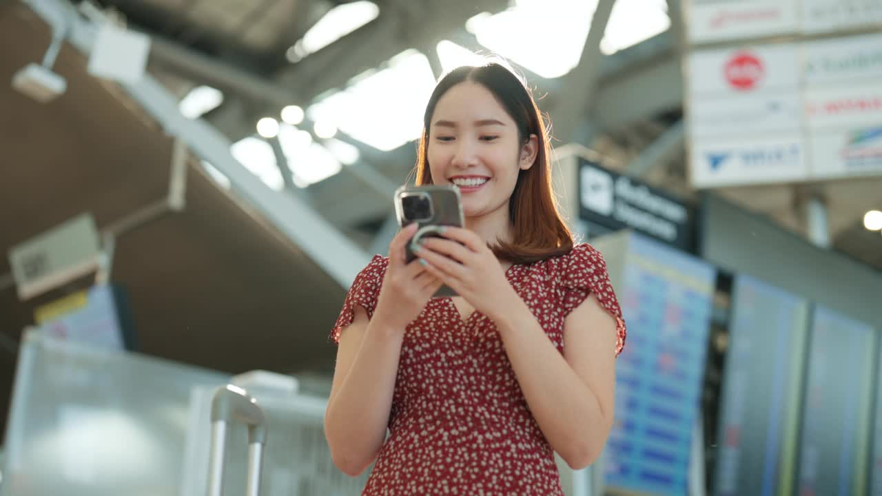 穿红裙子的亚洲女子在机场用智能手机给朋友发短信视频下载