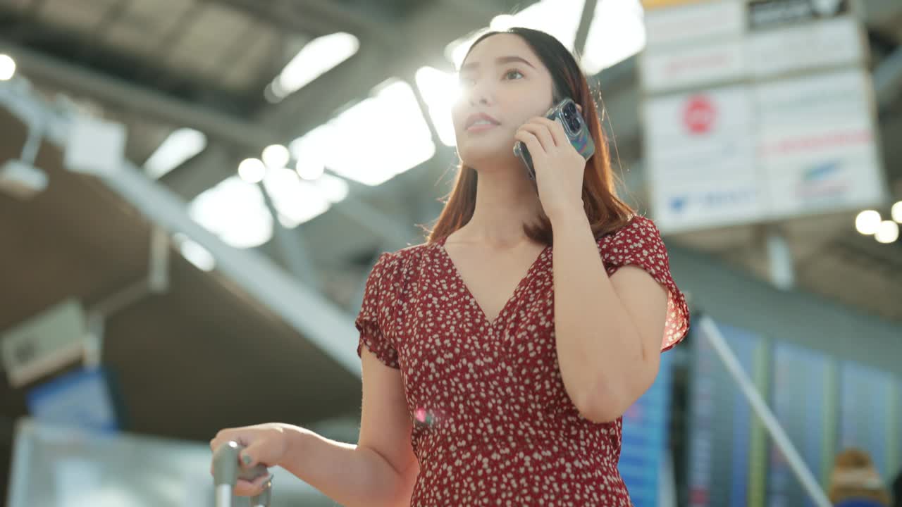 年轻的亚洲女子在繁忙的机场候机楼打电话，等待她的航班视频下载