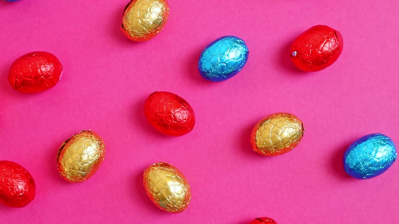 巧克力复活节彩蛋在一个彩色的包装在粉红色的背景。视频下载