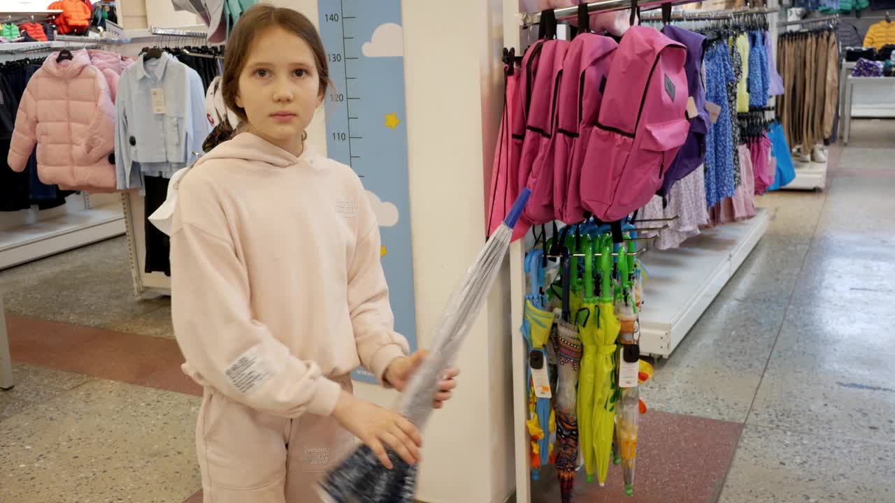 一个十几岁的女孩在商店里挑选一把伞。美丽的女孩在购物中心挑选雨伞。为坏天气做准备。购买。选择视频下载