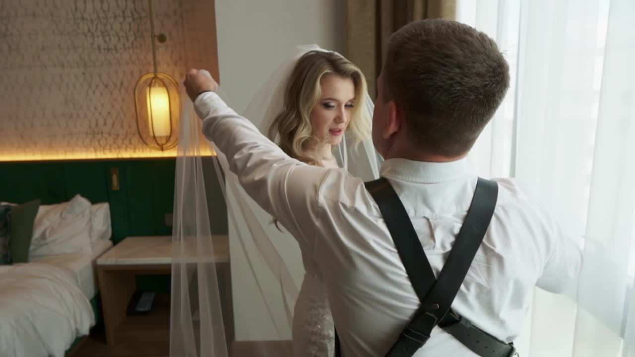 后台婚礼拍摄。身着婚纱、头戴面纱的新娘站在窗边。视频素材
