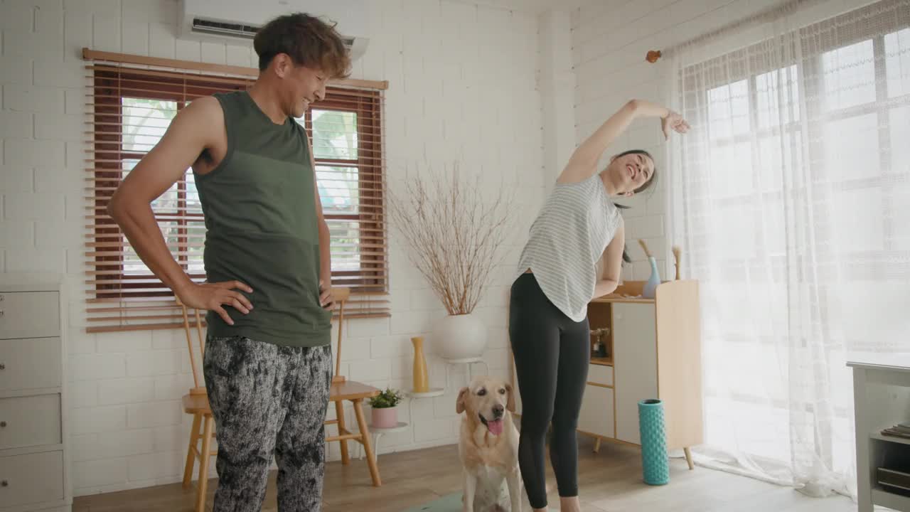 亚洲的成熟夫妇在家里和他们的狗一起在客厅做瑜伽或力量训练视频下载
