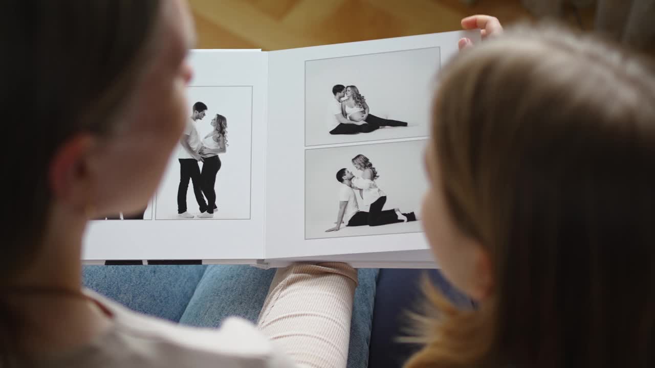 母女俩翻看一本有爸爸和怀孕妈妈照片的书。视频下载