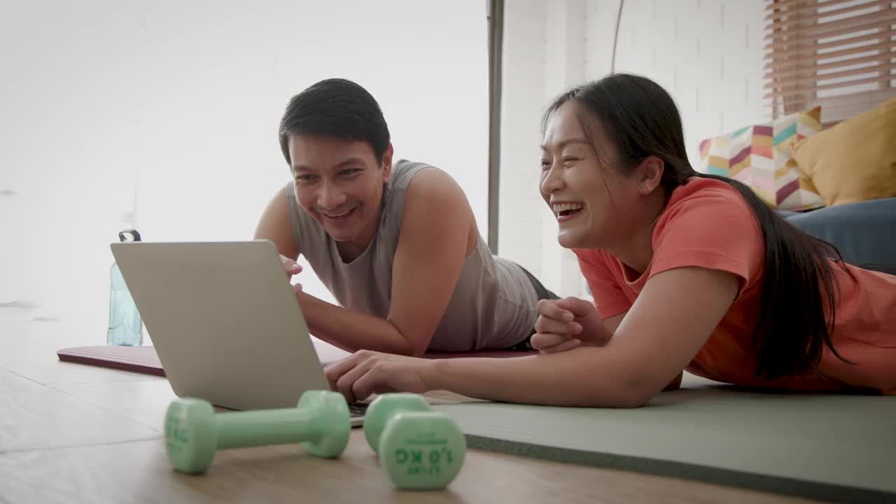 亚洲成年夫妇在家里一起做瑜伽或力量训练后使用笔记本电脑的照片视频下载