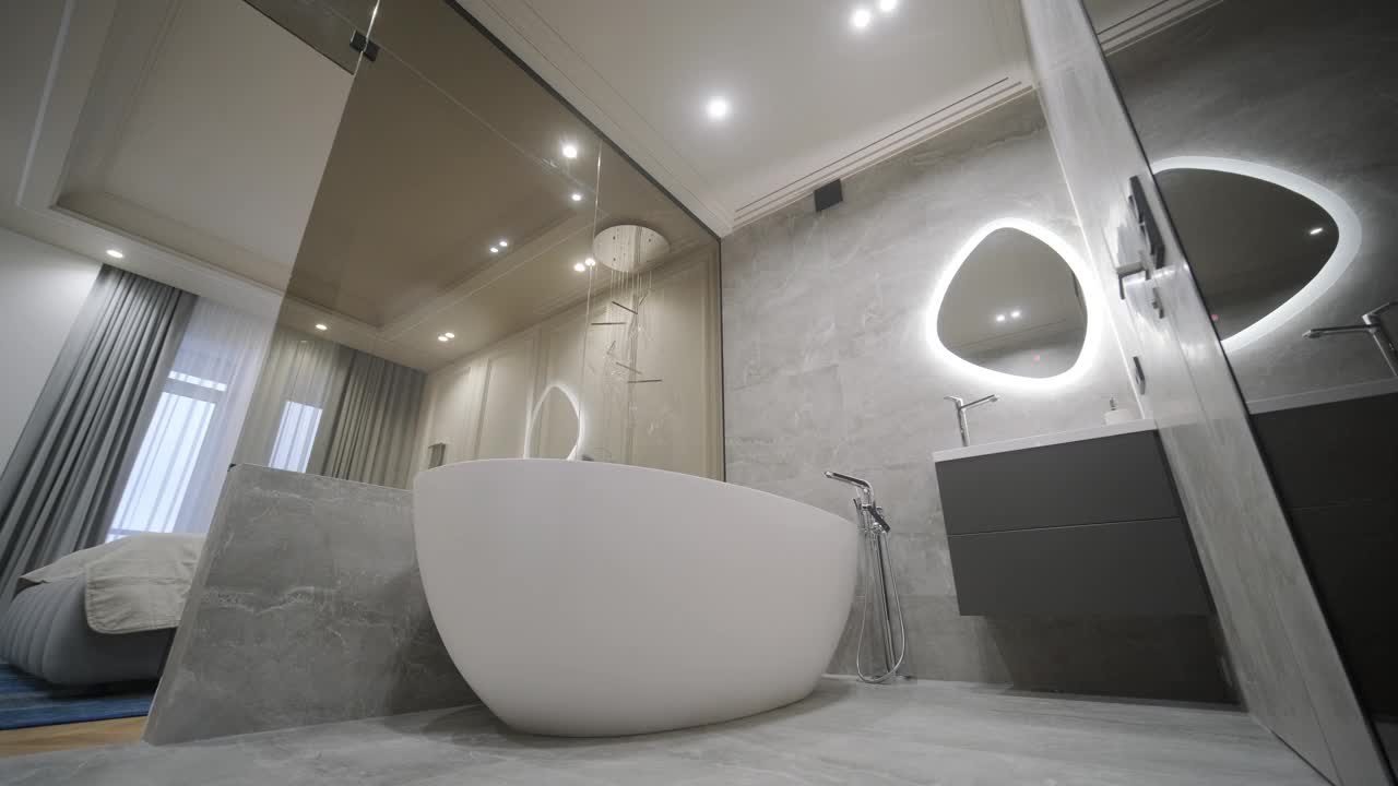 宽敞的浴室，一个独立的浴缸，大理石瓷砖，和一个背光镜子，反映了卧室的一瞥视频下载