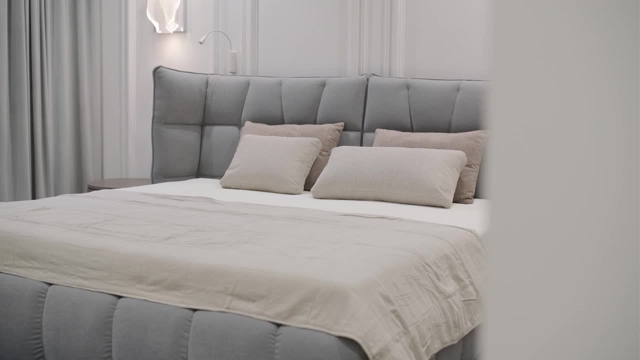 一个现代的卧室展示了一个大的软垫床与灰色色调的羽绒床头板，完成协调的床上用品和枕头视频下载