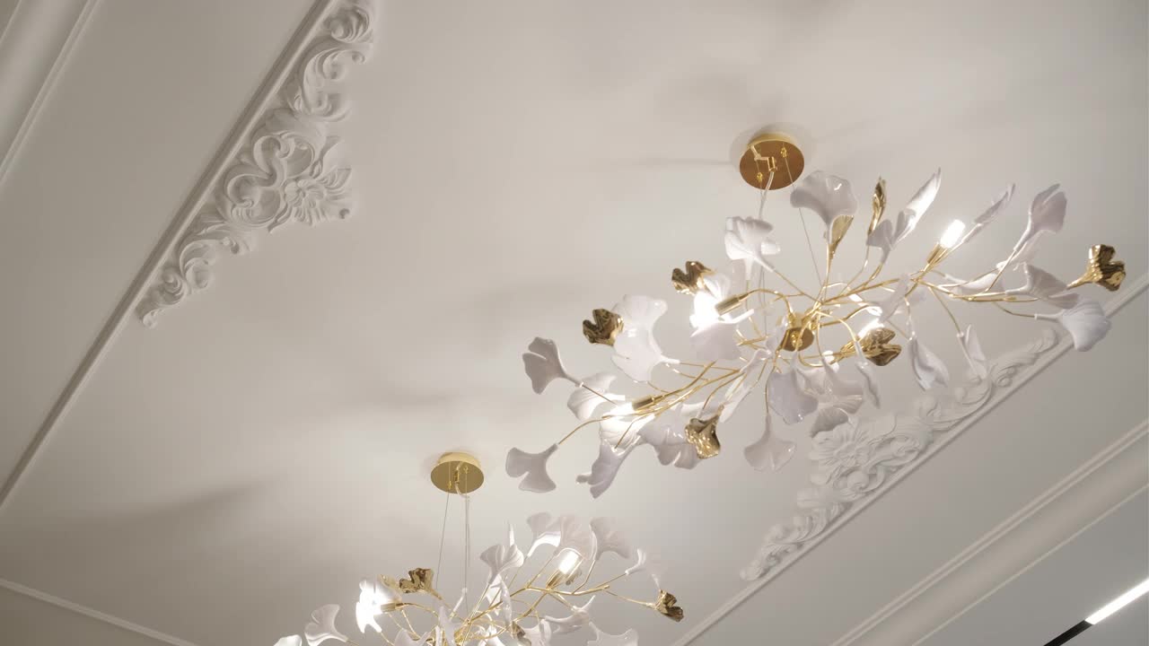 优雅的花吊灯与白色的花瓣和金色的茎照亮了豪华的内部。视频下载