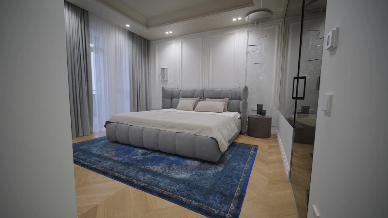 设计优雅的卧室，一个大的，簇绒床，丰富的蓝色地毯，经典的面板墙，和一个清晰的视野进入一个圆滑的，现代的浴室，反映了一个豪华和谐的生活空间。视频下载