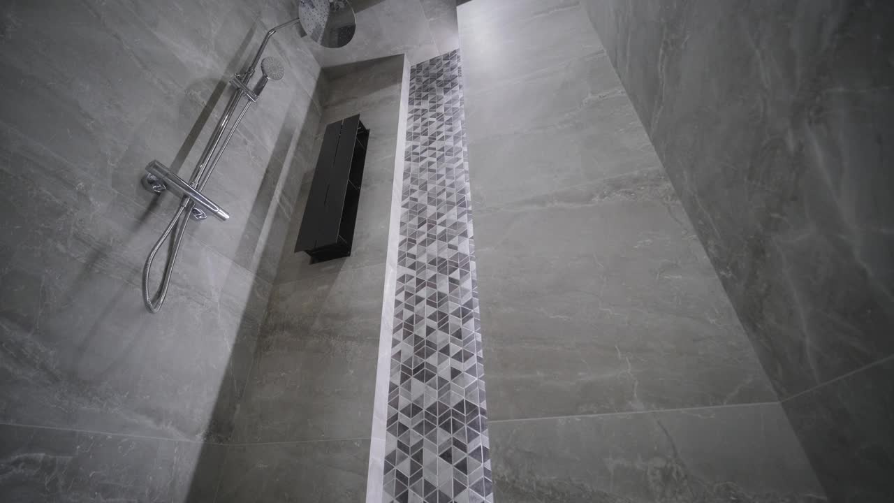 现代浴室设有极简主义的步入式淋浴间，带有几何图案的瓷砖条和光滑的固定装置，与灰色石墙相衬视频下载