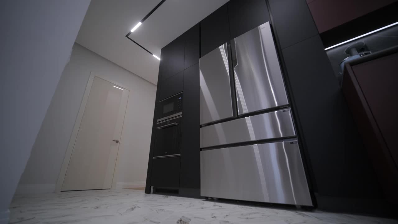 一个现代化的厨房，有光滑的黑色橱柜，不锈钢电器，在大理石地板的房间里集成了照明视频下载