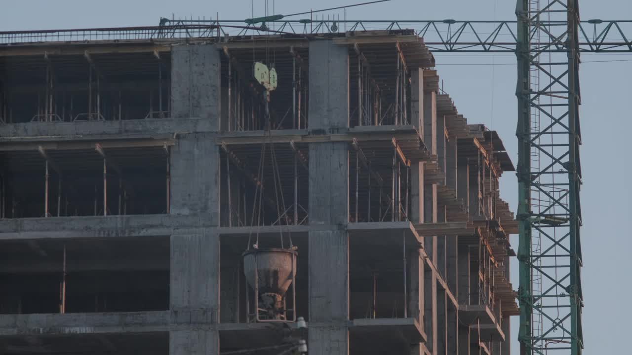 黄昏时拍摄的一座在建高层建筑的特写，可以看到混凝土结构和脚手架，旁边是一台起重机视频下载