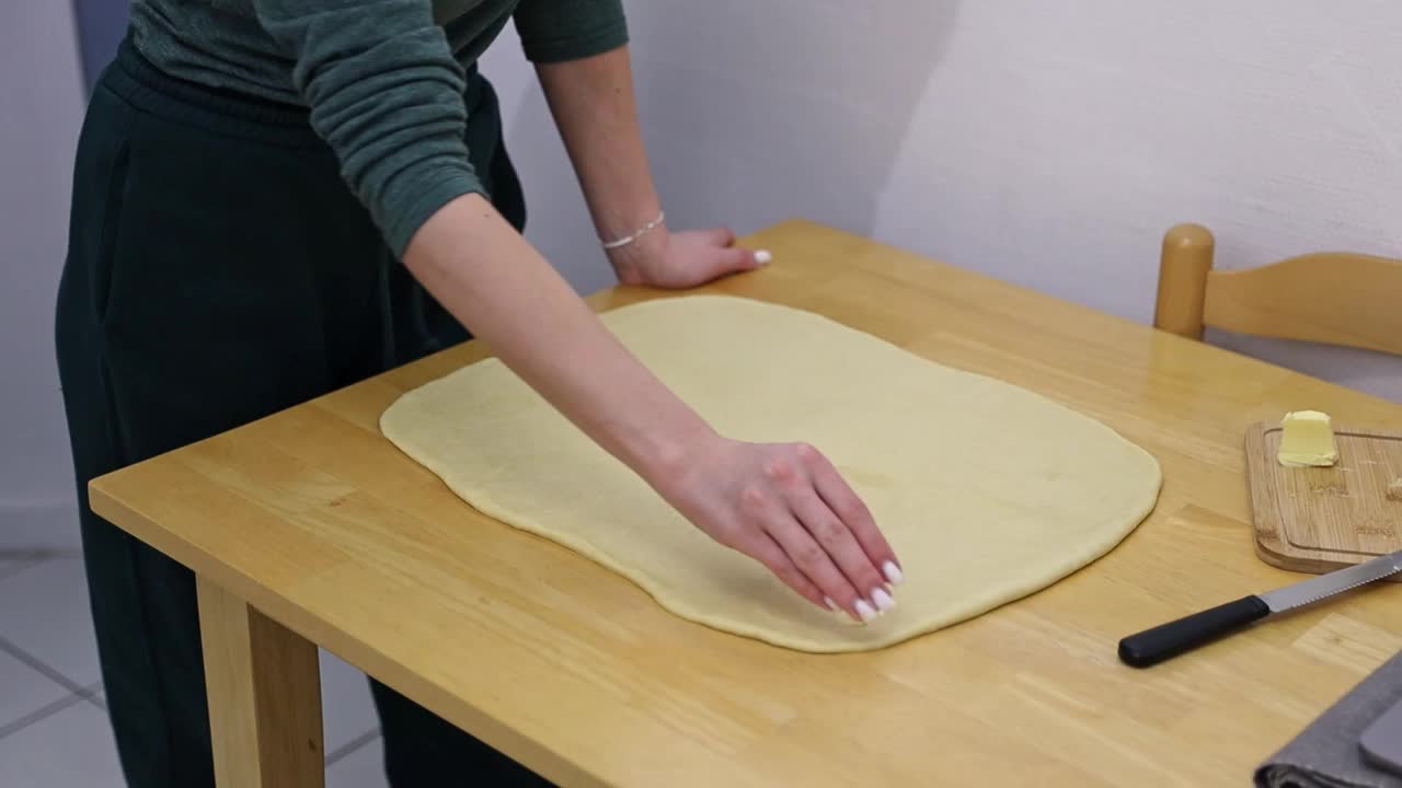 一个女孩把黄油涂在做肉桂的面团上。视频下载